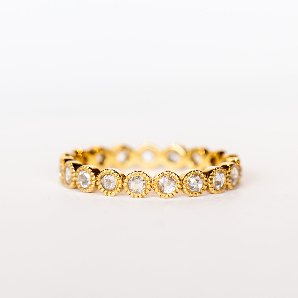 A yellow gold and diamond eternity band with rose cut round diamonds bezel set with milgrain edges.