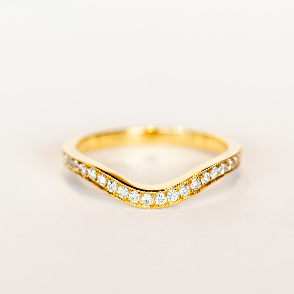 A contour curved rose gold wedding band with a row of petite diamonds along the top.
