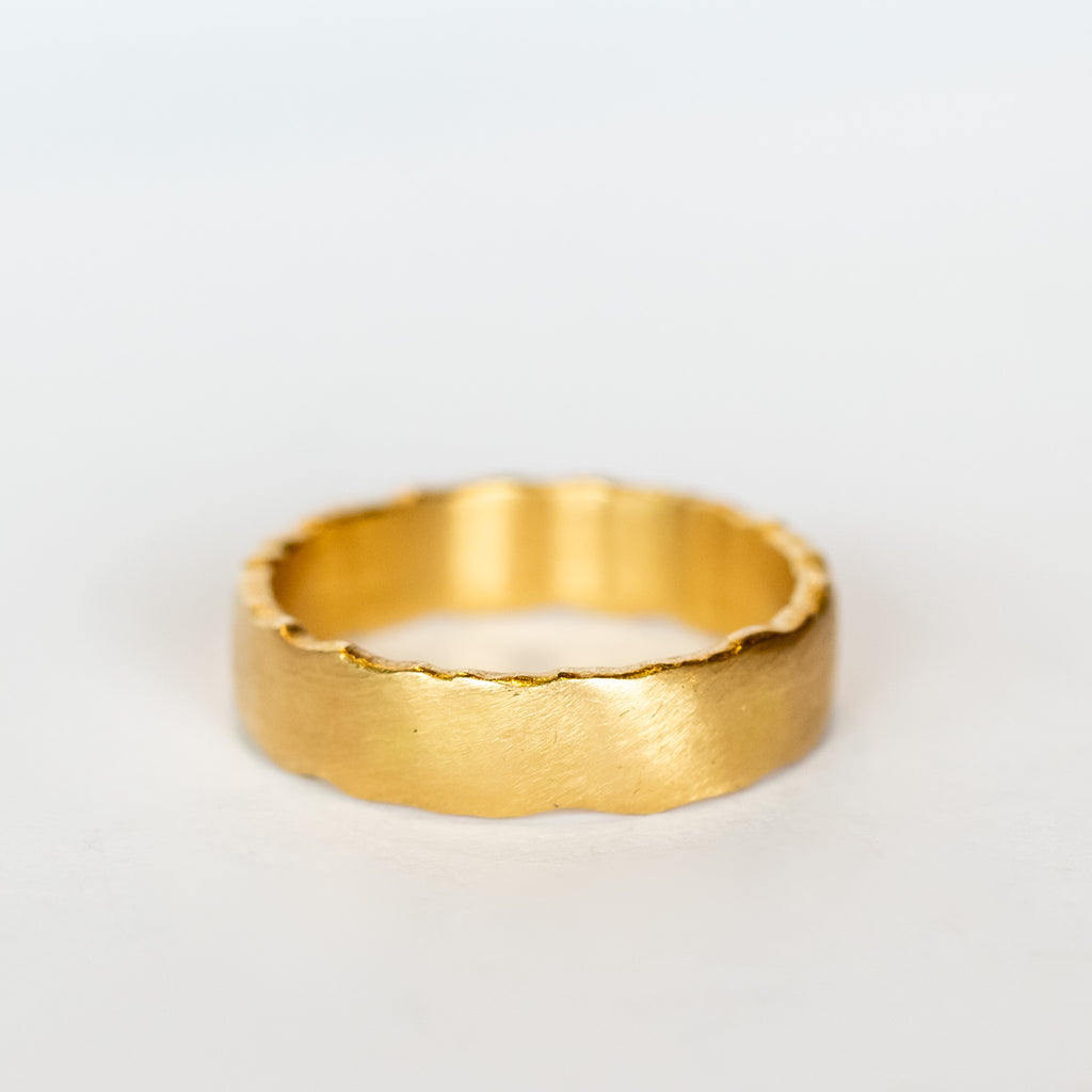 A wide, yellow gold wedding band with brushed matte finish and torn-paper like edges.