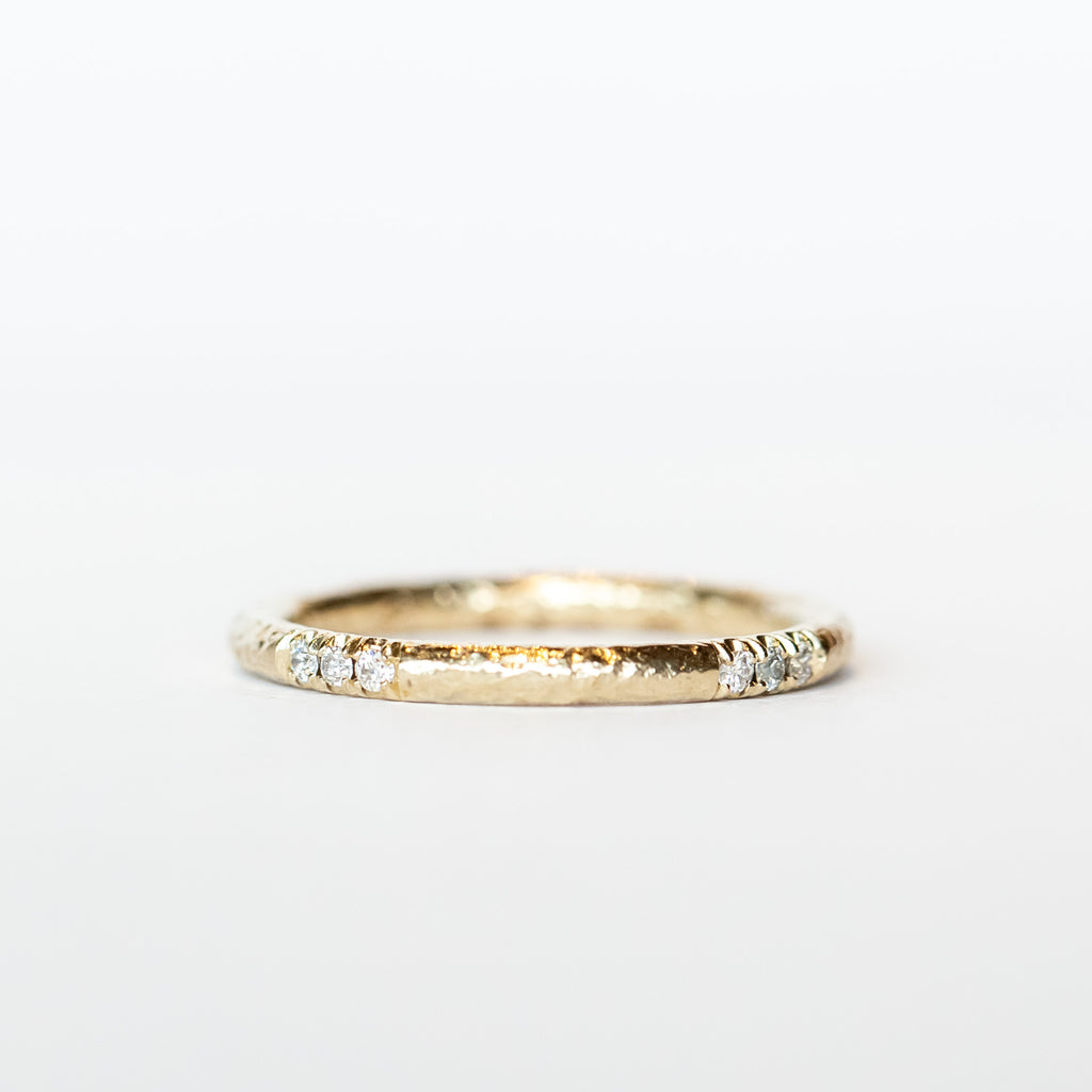 A white gold wedding band with a hammered texture and rows of three-diamonds inlaid in a spaced out design.