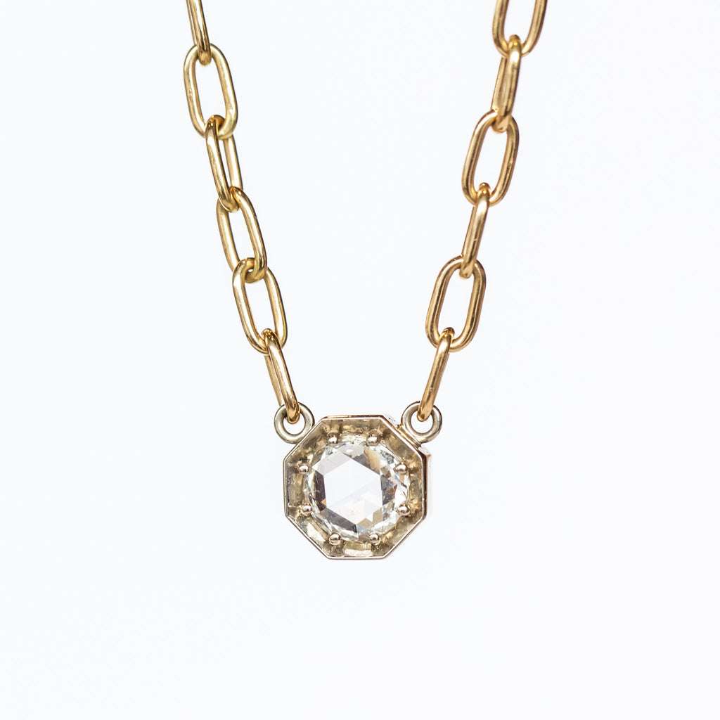 A rose cut diamond set in an octagonal white gold mounting centered on a yellow gold paperclip chain necklace.