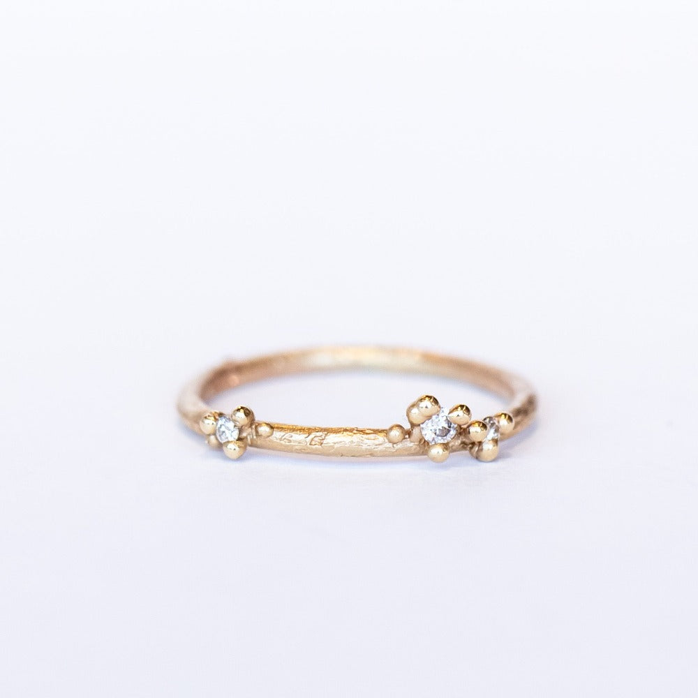 A delicate wedding band or stacking ring featuring white diamonds in two asymmetrical clusters set amongst granules of yellow gold.