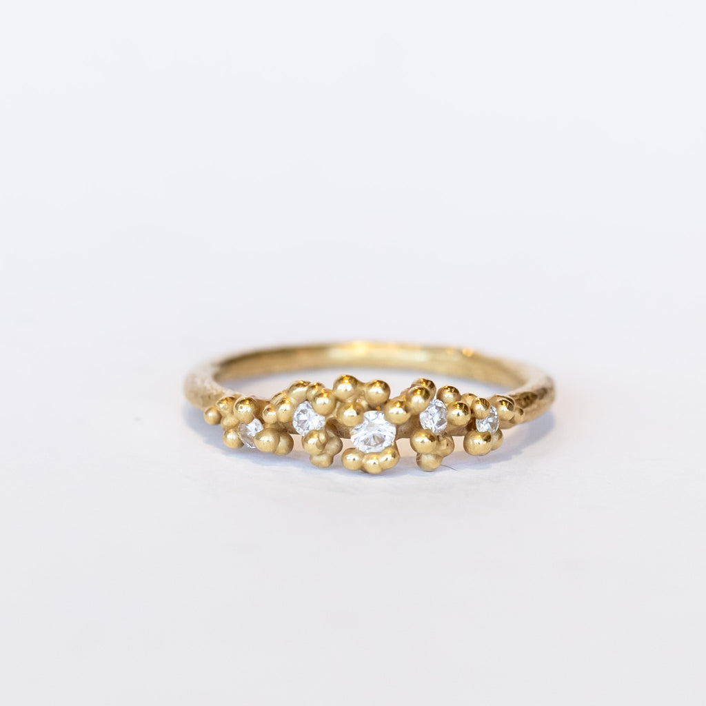 Unique diamond cluster engagement ring with golden granules, on a gently textured band.