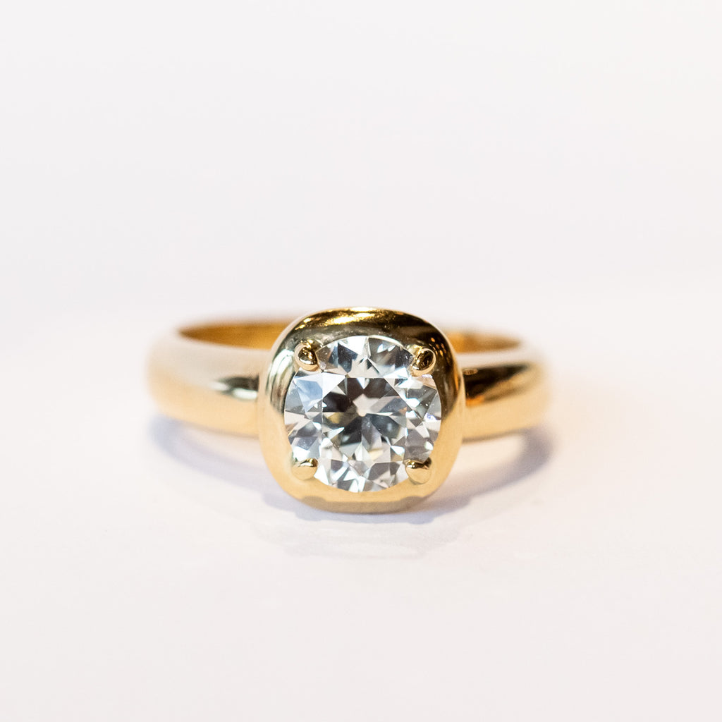 A chunky gold solitaire engagement ring featuring an old mine European cut diamond prong set into a cushion-like setting.