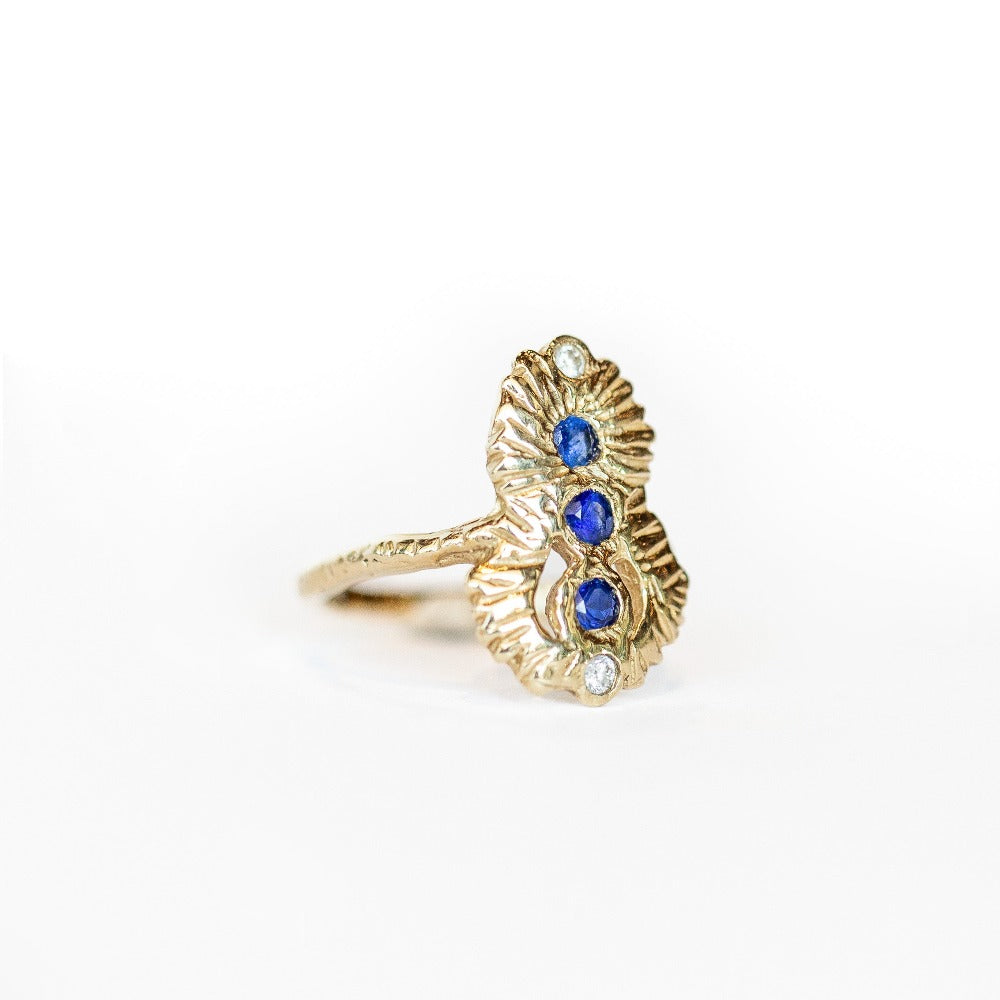 Side view of a Communion by Joy ring, hand carved from 14 karat yellow gold, it is set with three deep blue round sapphires and two white diamonds. 