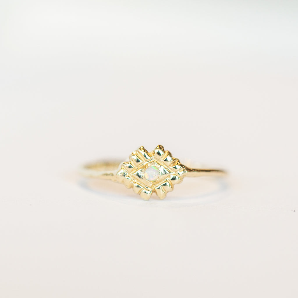 A petite gold Communion by Joy ring featuring a thin gold band, hand carved details and tiny opal.