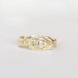 A hand-carved yellow gold band, approximately 4mm width, with an oval shaped top plate carved with an eye and a diamond set in its center. Top view.