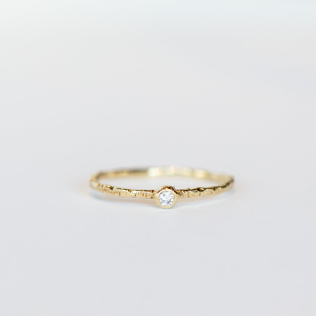 A thin yellow gold ring from Communion by Joy, featuring hand carved texture and bezel set with one tiny white diamond.