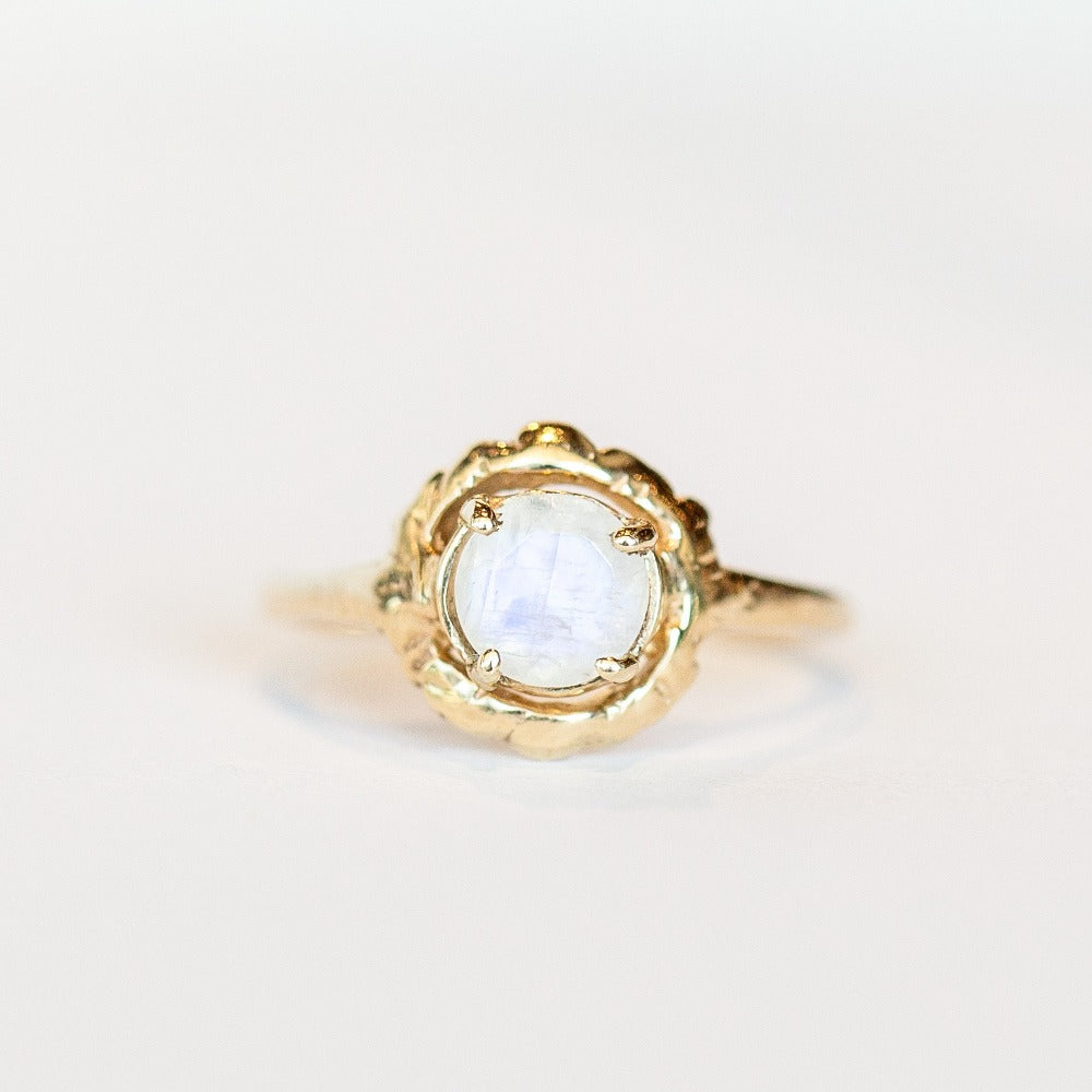 A hand carved yellow gold Communion by Joy ring featuring a thin band set with a faceted round moonstone.