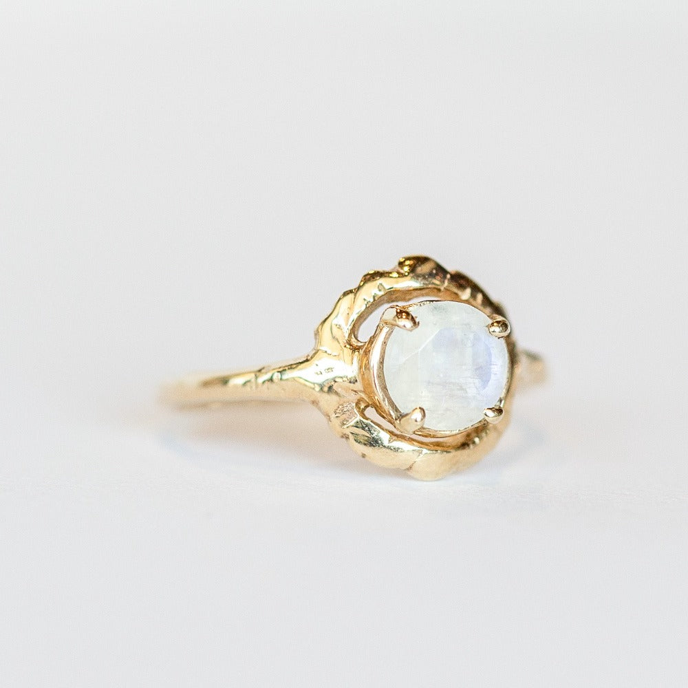 A hand carved yellow gold Communion by Joy ring featuring a thin band set with a faceted round moonstone.