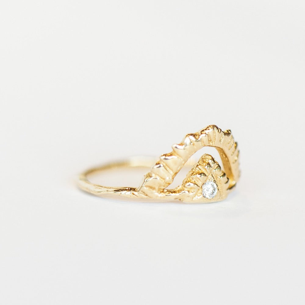 Slight side view of Communion by Joy ring. It's made of hand carved yellow gold, featuring an open pyramid shape on top, with one tiny diamond at the center, and a thin gold band.