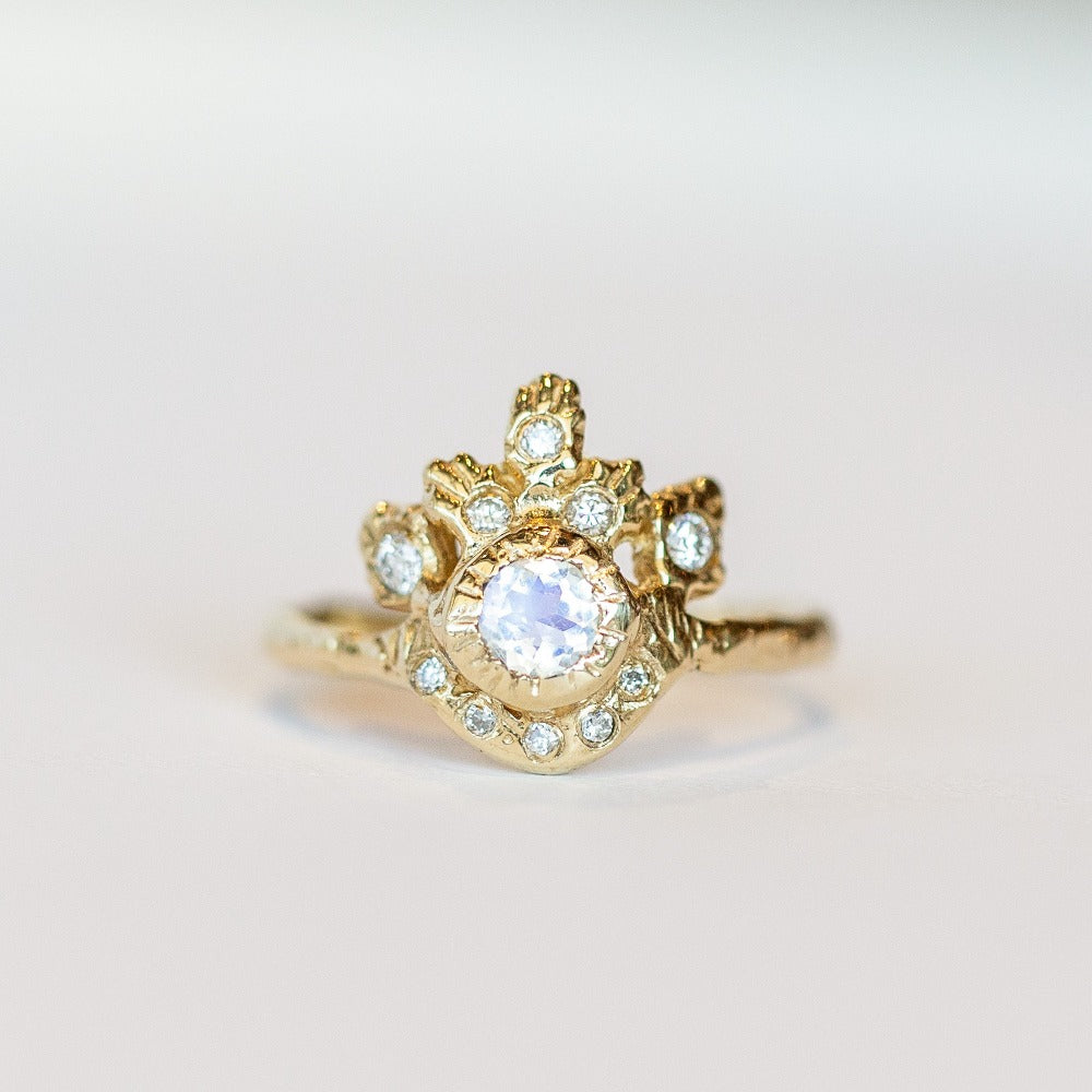 Front view of a hand-carved, yellow gold Communion by Joy ring featuring a round faceted moonstone surrounded by intricately detailed gold and white diamonds.