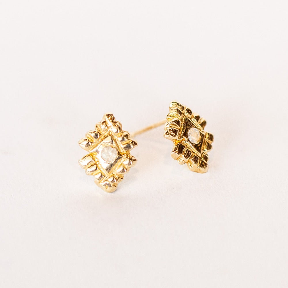 A pair of hand carved, diamond shaped yellow gold stud earrings from Communion by Joy, featuring small white moonstones.