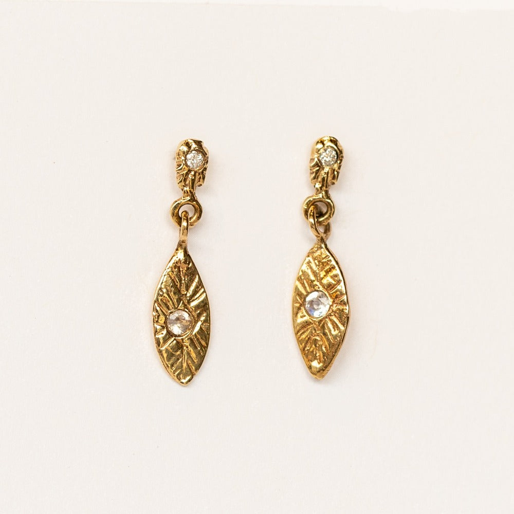 A pair of yellow gold petal-shaped drop earrings from Communion by Joy. They feature four tiny white diamonds and hand carved details.