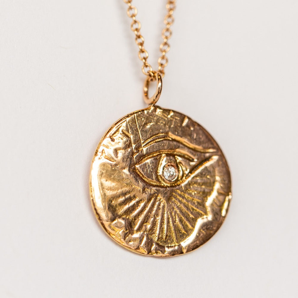 A carved eye medallion necklace with a petite diamond set in rose gold from Communion by Joy.