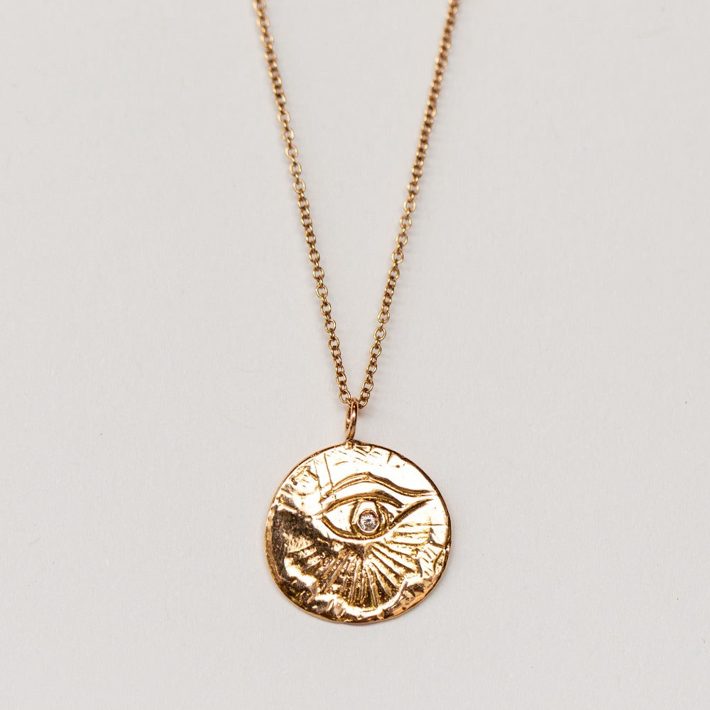 A carved eye medallion necklace with a petite diamond set in rose gold from Communion by Joy.