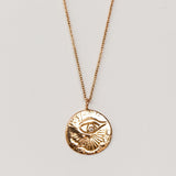 A carved eye medallion necklace with a petite diamond set in rose gold from Communion by Joy.