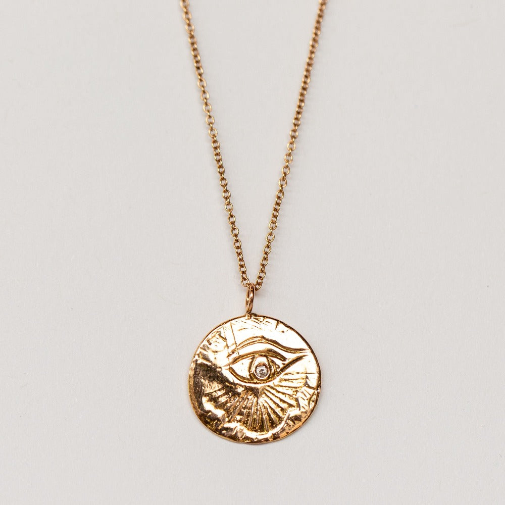 A carved eye medallion necklace with a petite diamond set in rose gold from Communion by Joy.