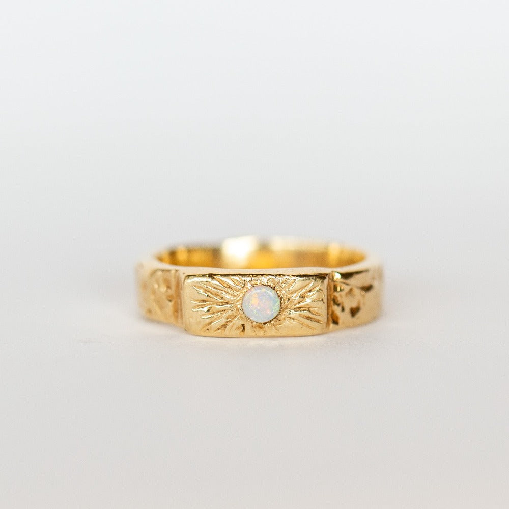 Front view of a wide, hand carved yellow gold band from Communion by Joy. It features a white opal.