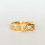 Slight side view of a wide, hand carved yellow gold band from Communion by Joy. It features a white opal.