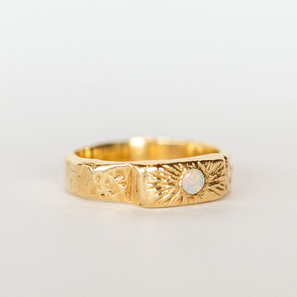 Slight side view of a wide, hand carved yellow gold band from Communion by Joy. It features a white opal.