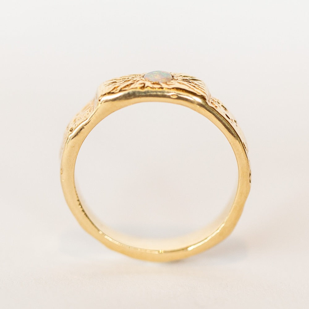 Side profile view of a wide, hand carved yellow gold band from Communion by Joy. It features a white opal.