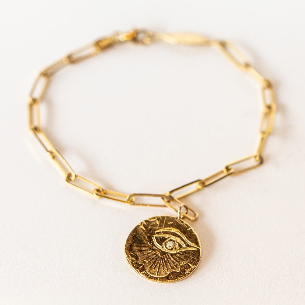 In this Communion by Joy bracelet, a hand-carved eye of love medallion hangs from an on-trend paperclip chain bracelet in 14 karat yellow gold. It's set with a single diamond.