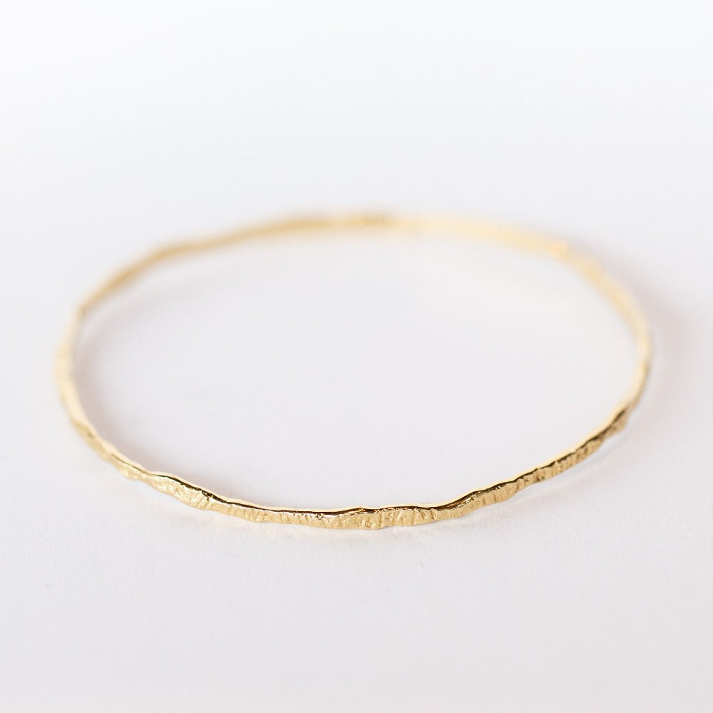 A thin, hand-carved yellow gold bangle bracelet from Communion by Joy.