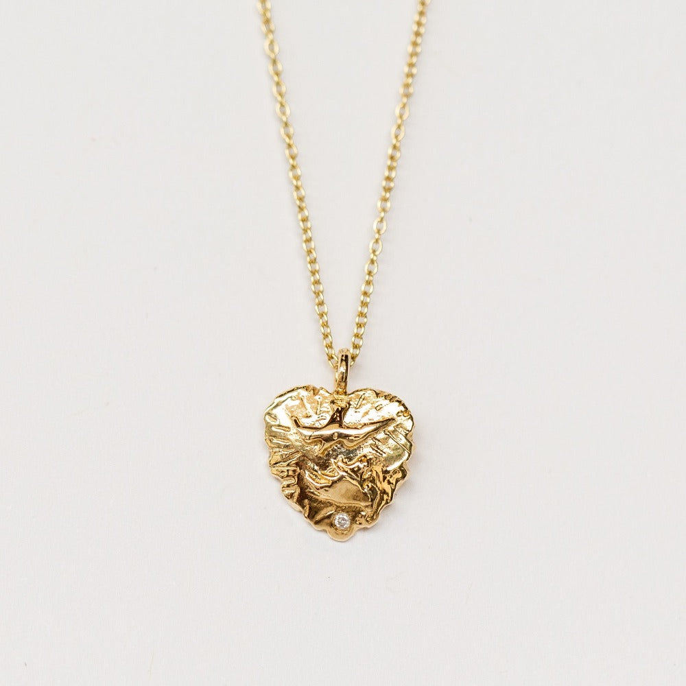 A hand carved gold heart pendant from Communion by Joy featuring a dove and tiny white diamond.