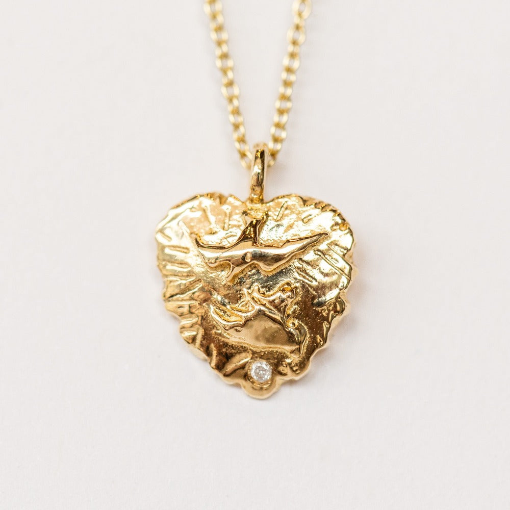 A hand carved gold heart pendant from Communion by Joy featuring a dove and tiny white diamond.