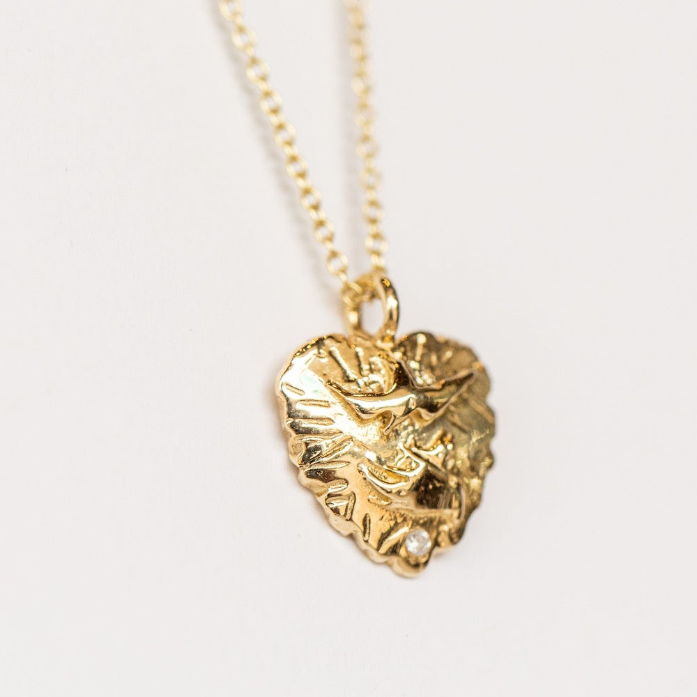 A hand carved gold heart pendant from Communion by Joy featuring a dove and tiny white diamond.