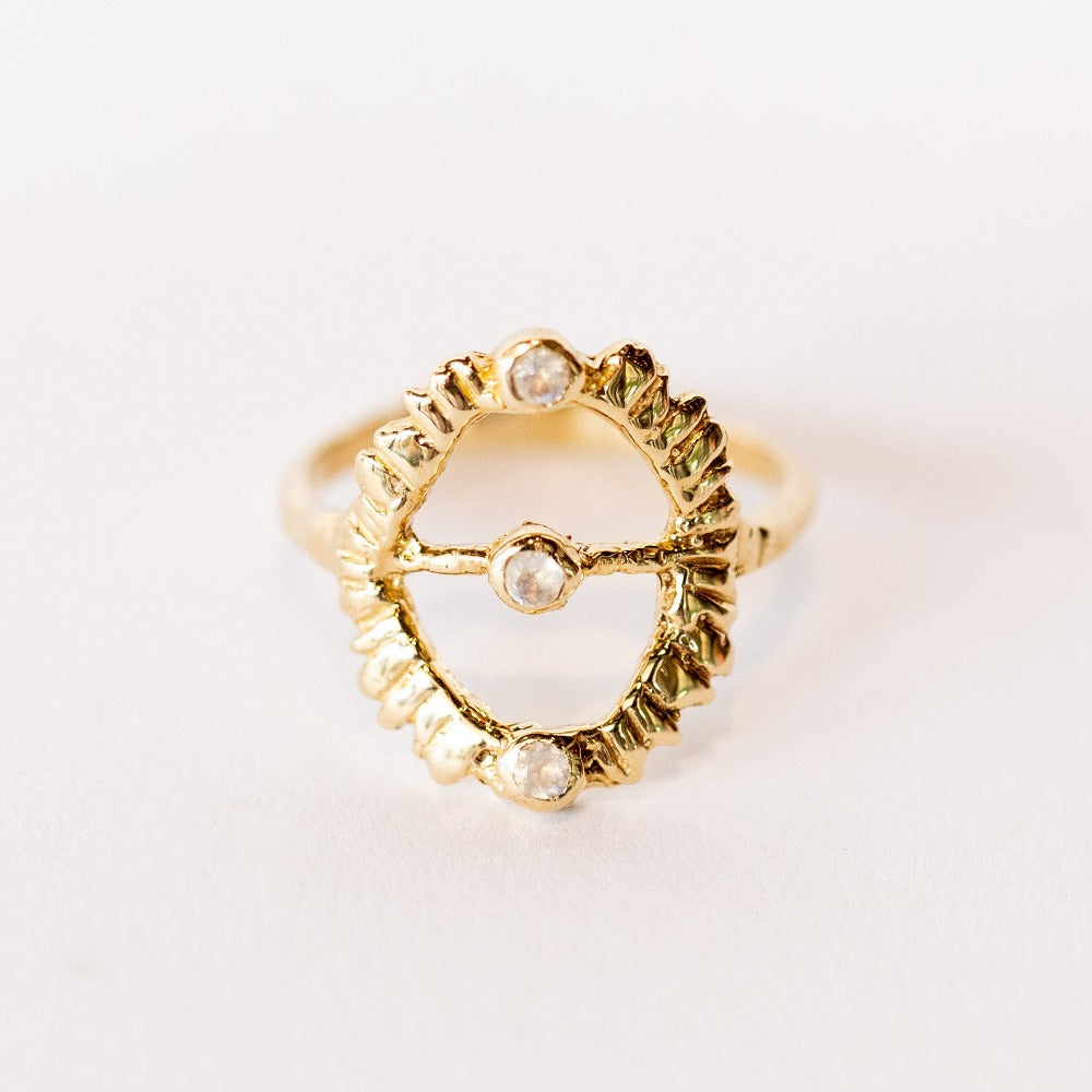 Top view of a hand carved yellow gold Communion by Joy ring. It features a thin band and open top, oval design set with three tiny moonstones.