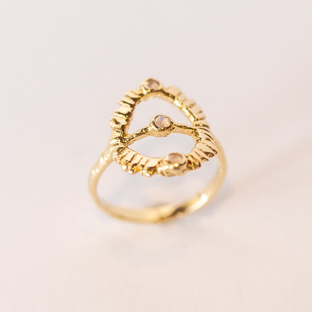 Angled view of a hand carved yellow gold Communion by Joy ring. It features a thin band and open top, oval design set with three tiny moonstones.
