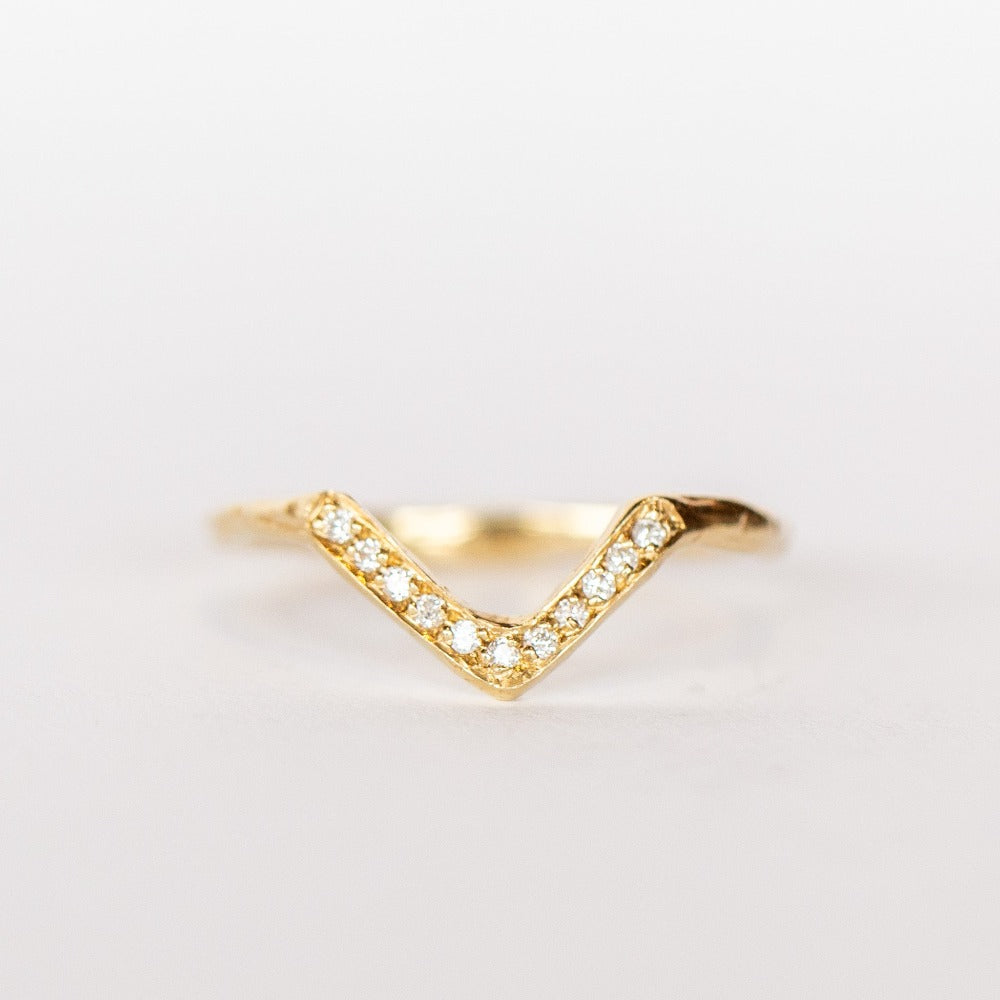 A yellow gold contour band from Communion by Joy, in a triangular peaked design, set with tiny white pave diamonds.