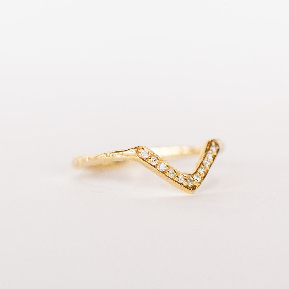 A yellow gold contour band from Communion by Joy, in a triangular peaked design, set with tiny white pave diamonds.