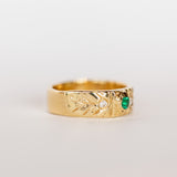 A wide gold band with hand carved detailing set with a center round emerald flanked by two white diamonds.