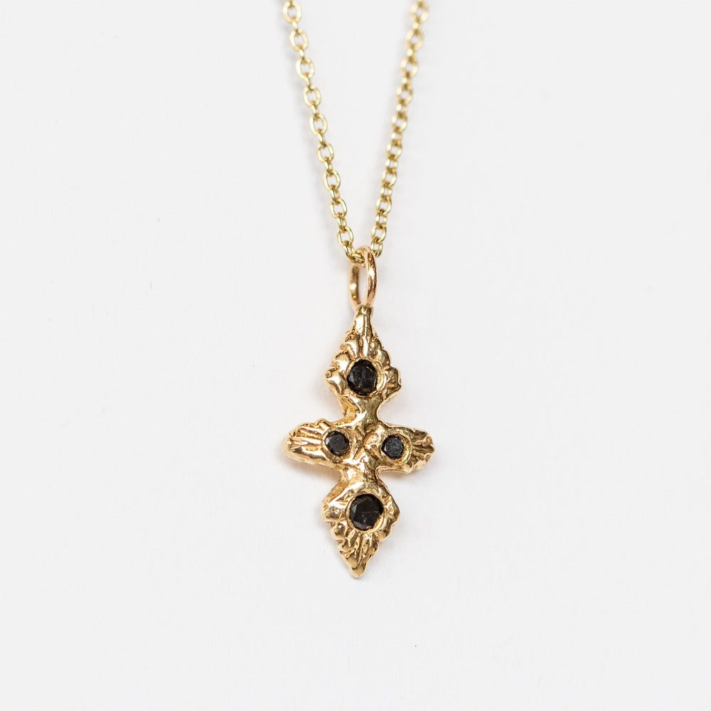 A hand carved yellow gold cross necklace set with black diamonds from Communion by Joy.