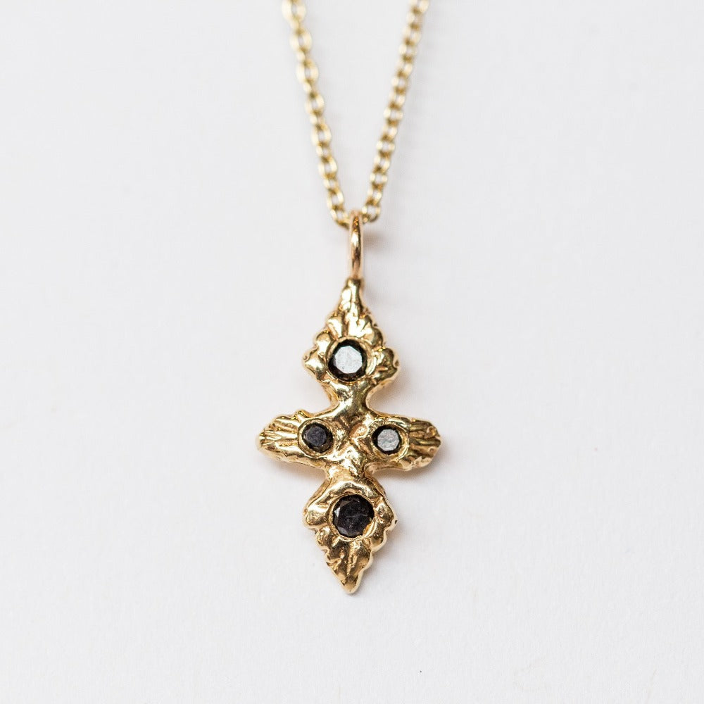 A hand carved yellow gold cross necklace set with black diamonds from Communion by Joy.