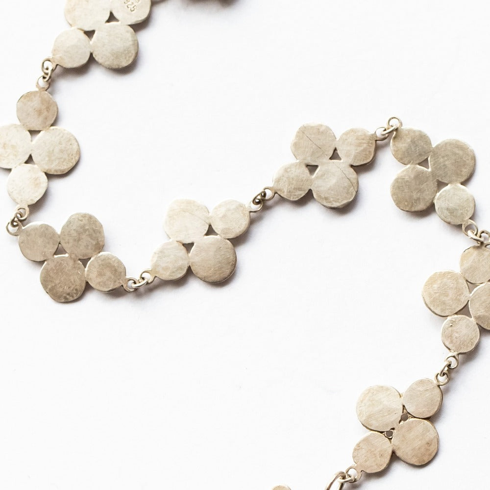 A chain bracelet featuring eight flat, cluster-shaped, hammered, sterling silver links joined with a lobster clasp and enhanced with a single matching clasp charm.