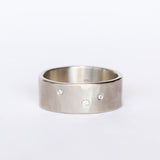 A wide, hammered white gold band with a brushed finish, set with three tiny scattered champagne diamonds.