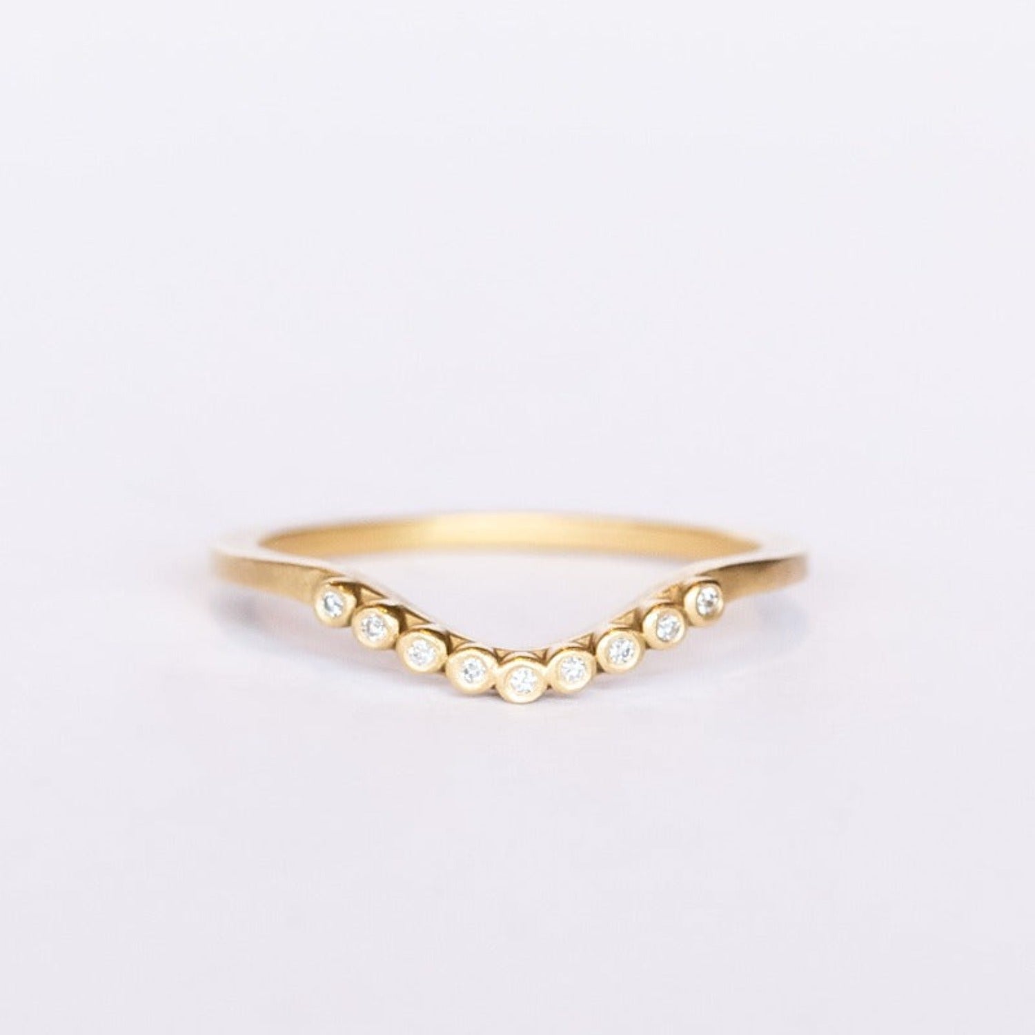 A dainty, yellow gold contour wedding band set with bezel set diamonds. Top view.