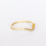 A dainty, yellow gold contour wedding band set with bezel set diamonds. side angle view.