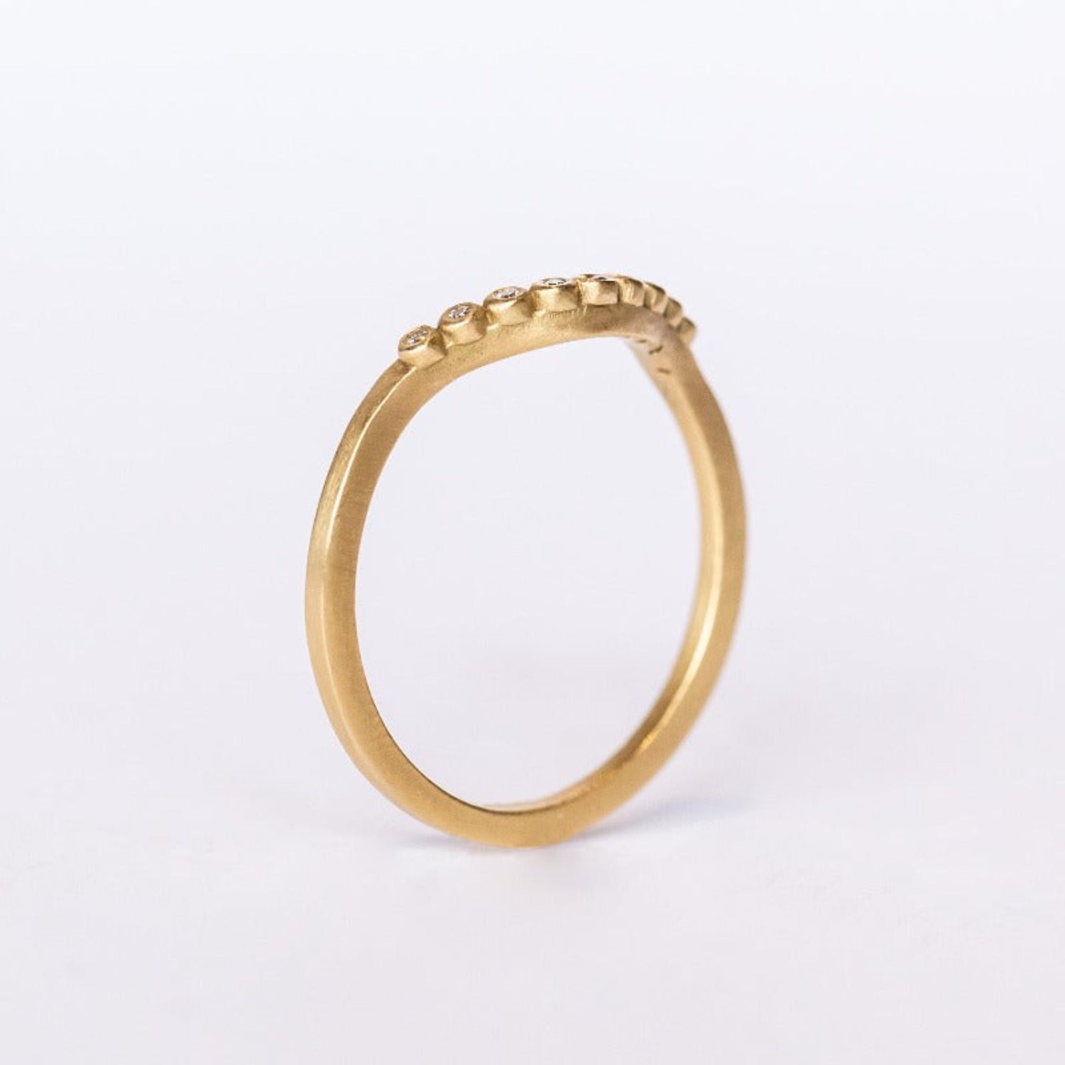 A dainty, yellow gold contour wedding band set with bezel set diamonds. Side profile view.
