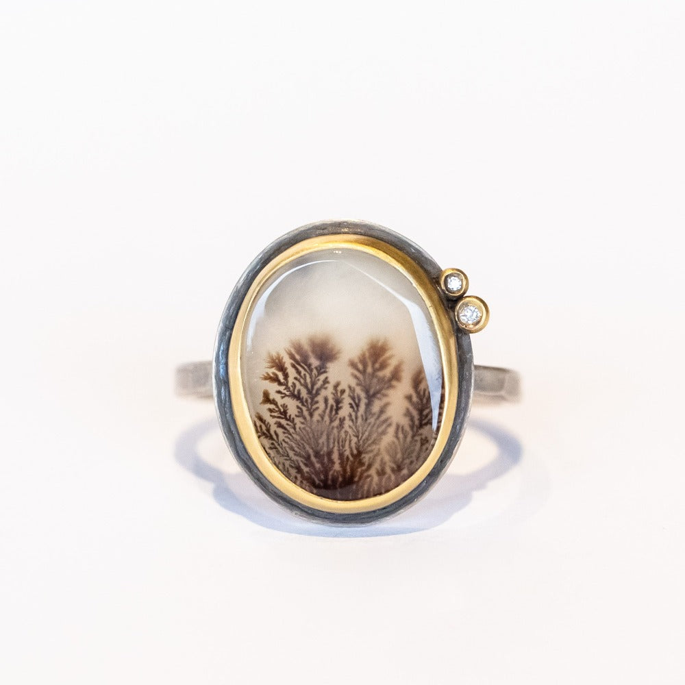 An oval shaped dendritic agate ring with two tiny diamond accents. Set in yellow gold bezel with sterling silver ring. Front view.