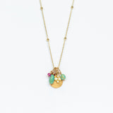 A yellow gold chain necklace with small gold spaced out beads and a handful of charms including a tiny ruby, a hammered gold disc, a diamond clover, and two turquoise beads.