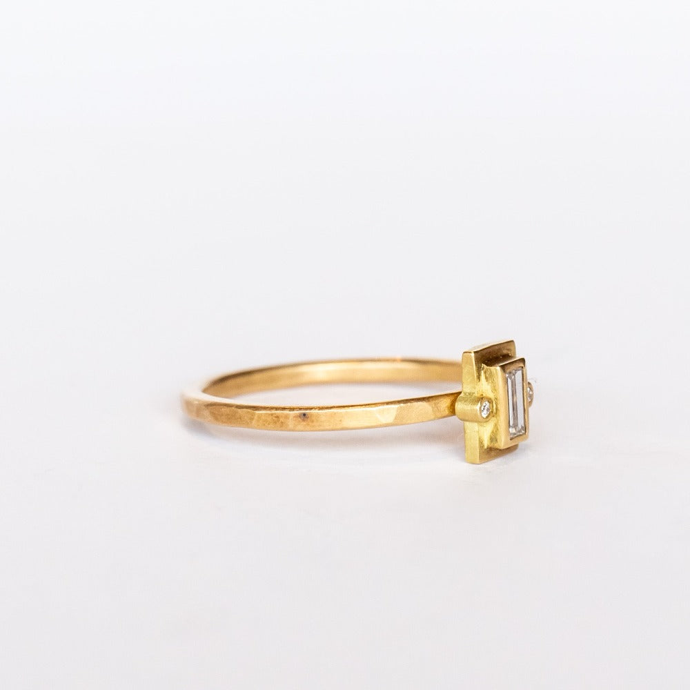 A thin hammered gold ring set with a tiny, bezel-set baguette diamond flanked by two tiny round diamonds.