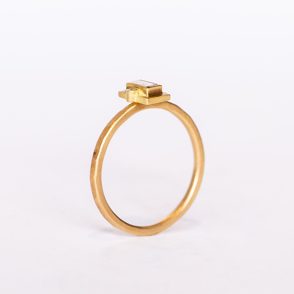 A thin hammered gold ring set with a tiny, bezel-set baguette diamond flanked by two tiny round diamonds.