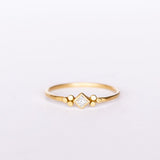 A thin gold ring featuring a kite-set princess cut diamond bezel set in yellow gold flanked by tiny dot trios.