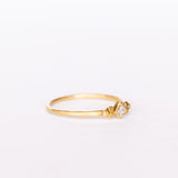 A thin gold ring featuring a kite-set princess cut diamond bezel set in yellow gold flanked by tiny dot trios.