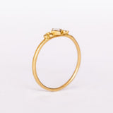 A thin gold ring featuring a kite-set princess cut diamond bezel set in yellow gold flanked by tiny dot trios.